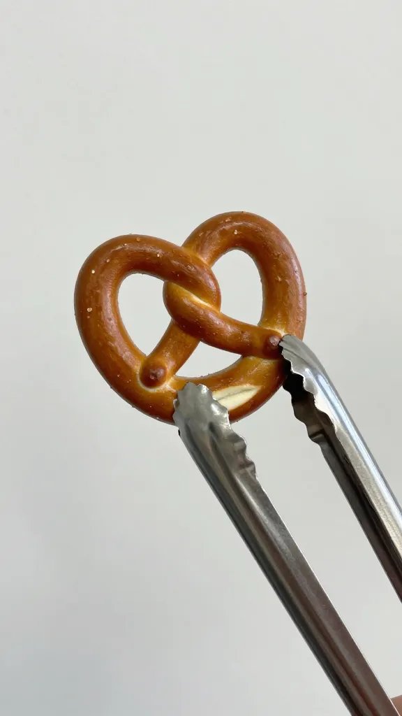 stainless steel tongs gripping one browned pretzel bite