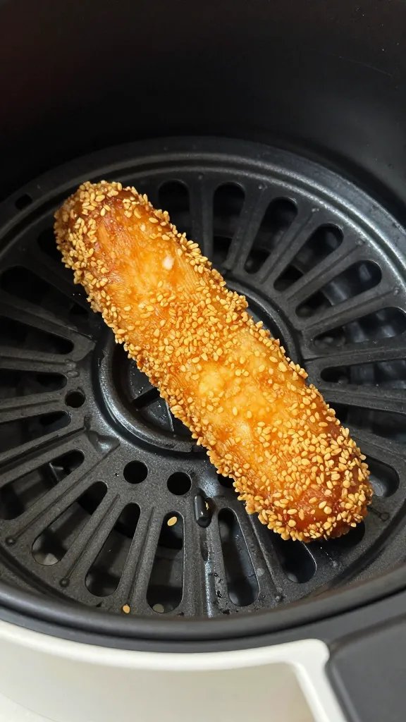 air fryer basket with one crispy chicken strip, closeup