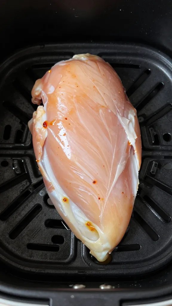 overhead shot of one seasoned raw chicken breast before air frying