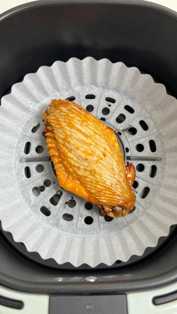 single chicken wing resting on parchment-lined air fryer basket