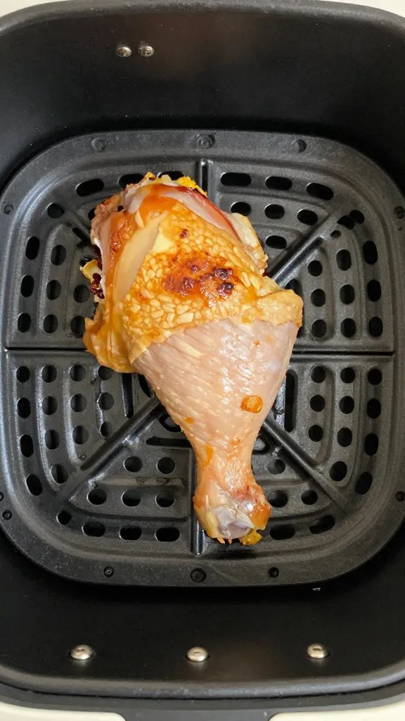air fryer basket with one cooked chicken thigh, top-down
