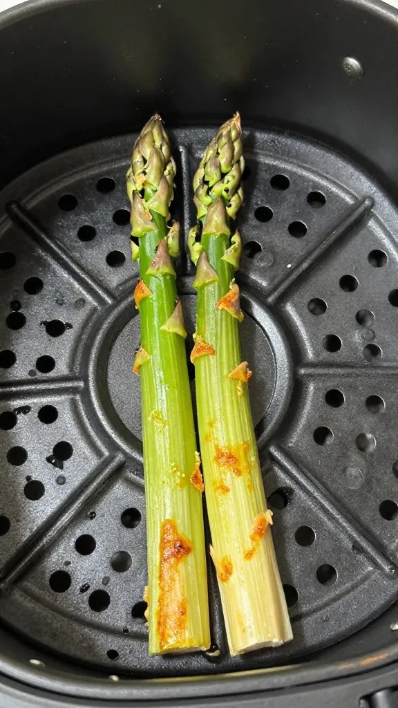 single asparagus spear in air fryer basket, golden edges