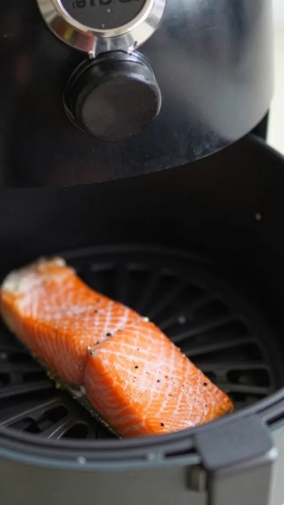 Air fryer basket handle closeup with salmon portion inside (blurred)