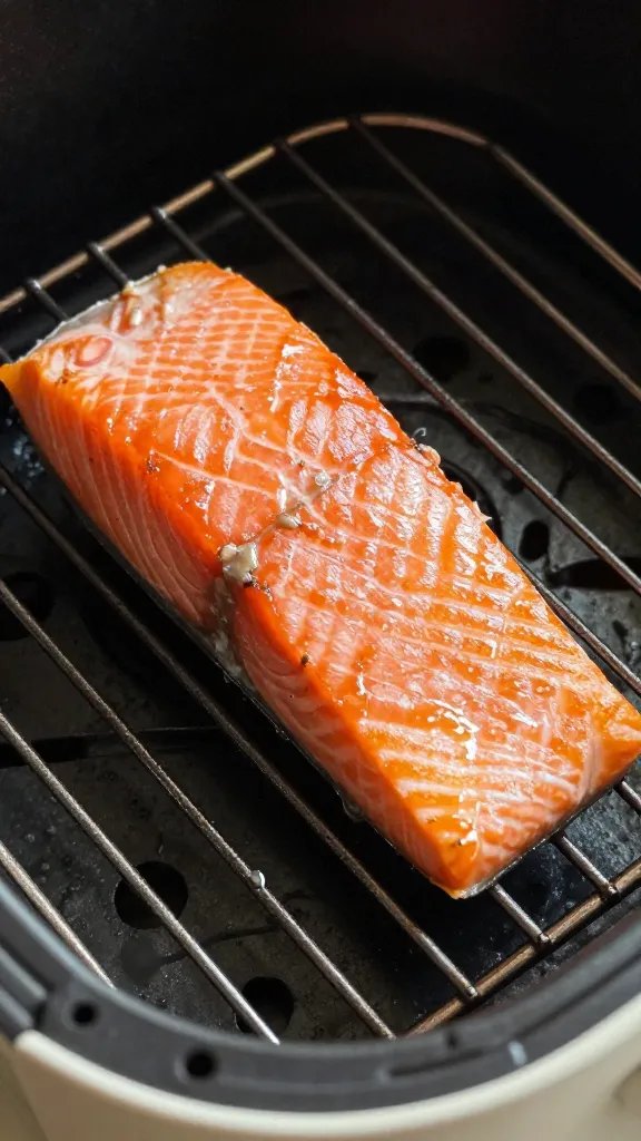 Air fryer rack with one salmon filet glistening under light