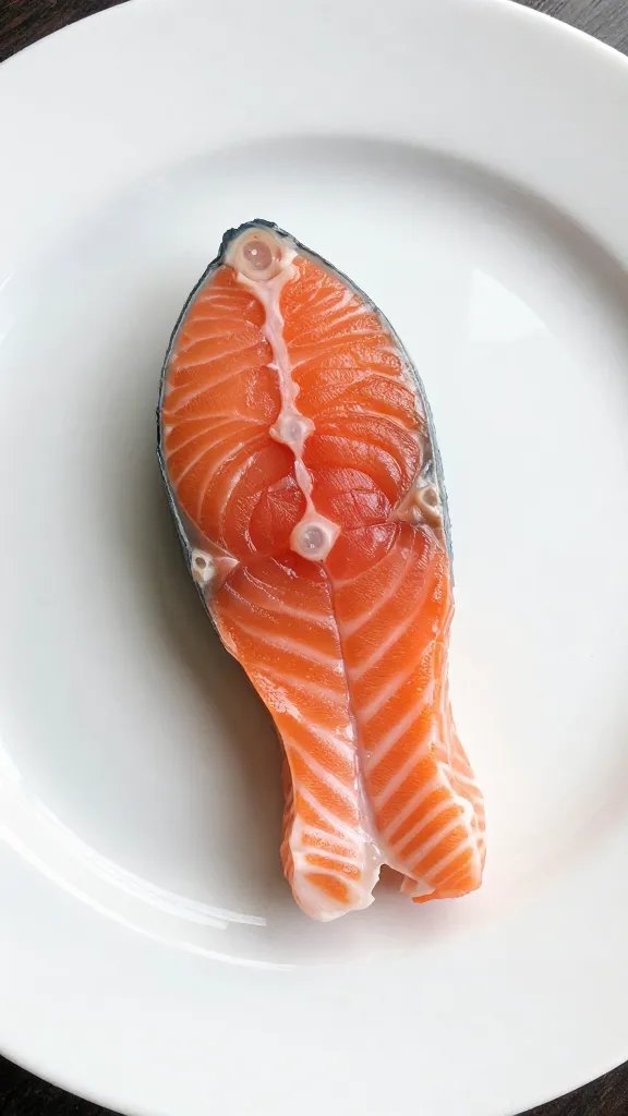Single salmon bite on white ceramic plate, glossy glaze